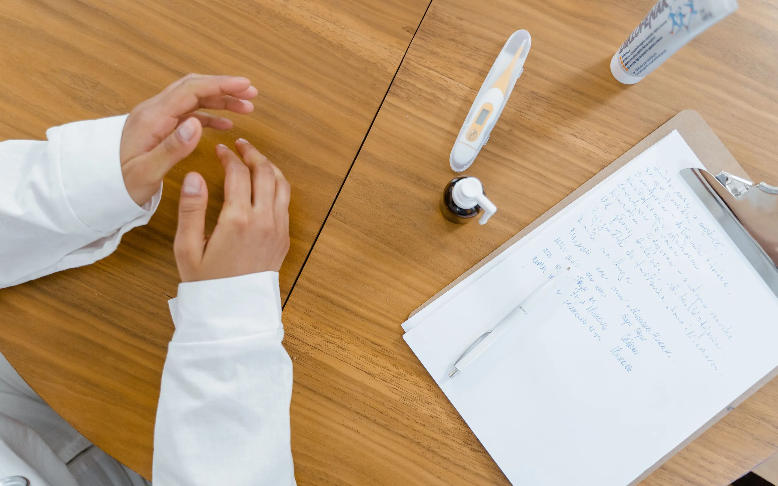 Bureau de consultation avec notes, thermomètre et mains d’un soignant